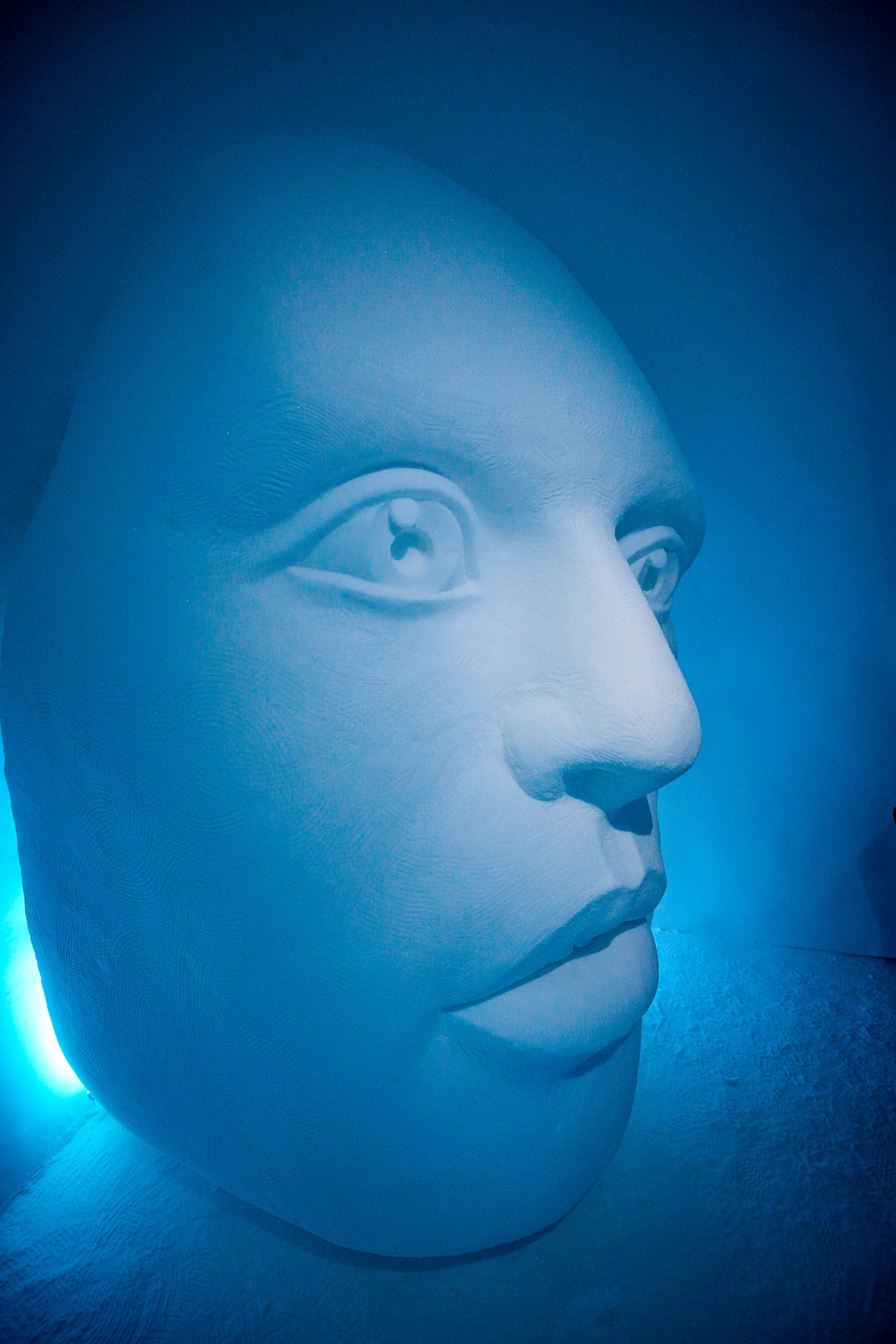 Sculpted ice face lit in deep blue at a Nordic ice hotel